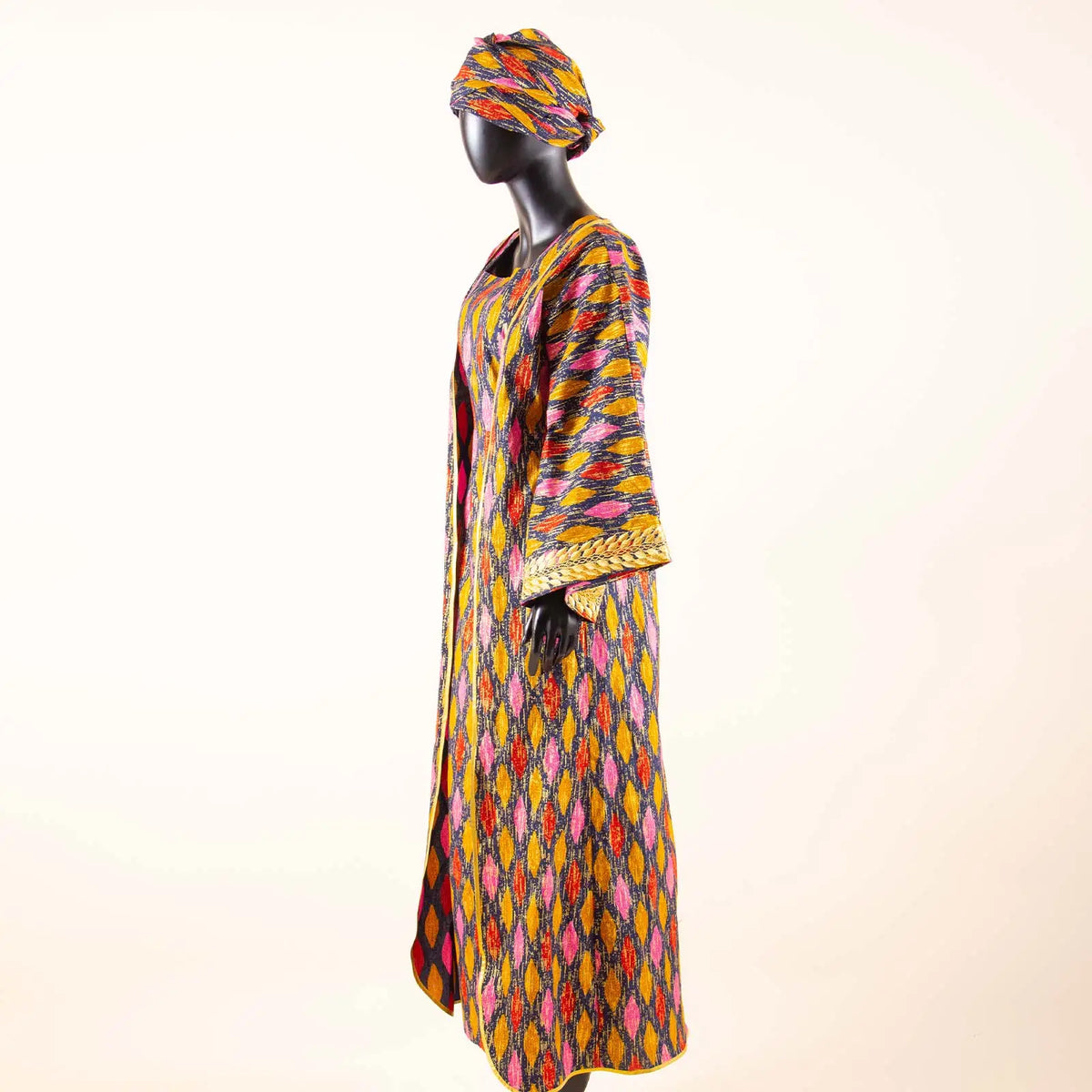 Mannequin wearing a colorful patterned dress and headscarf on a white background
