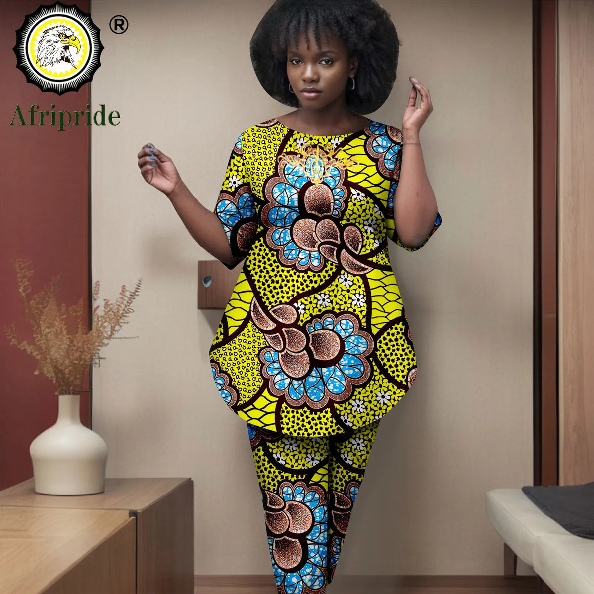 Woman wearing a colorful African print outfit in a room with decor elements.